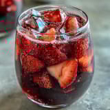 Two tall glasses filled with pink fruity Strawberry Açaí Refresher, garnished with strawberry slices and mint leaves for a cooling summer drink.