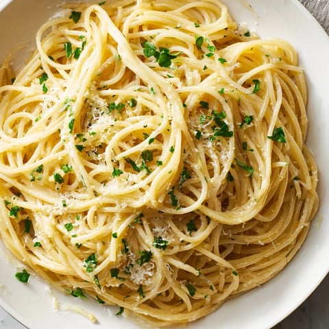 A close-up of Lemon Butter Pasta Light on a white plate, showing capellini strands coated in a silky, glossy sauce flecked with fresh parsley and lemon zest.