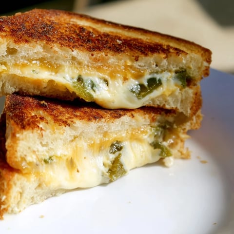 Golden-brown grilled cheese sandwich slices oozing melted cheddar and cream cheese with fresh diced jalapeños on a plate.