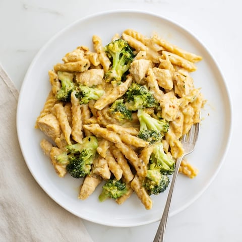 Creamy Chicken Broccoli Cheddar Pasta served hot in a skillet, with tender chicken pieces and bright green broccoli florets coated in a velvety cheese sauce.