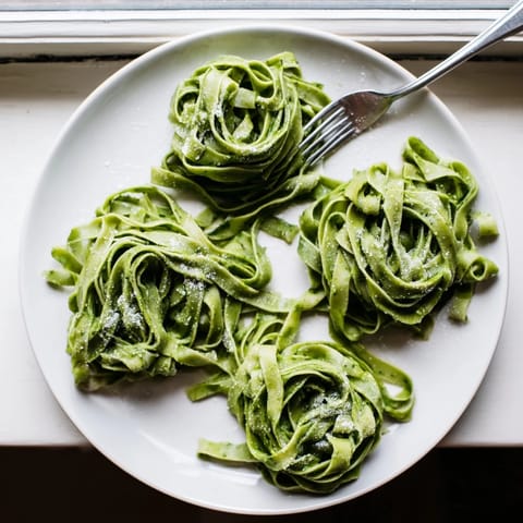 A vibrant green spinach pasta dough ball rests on a floured wooden countertop, ready for rolling.