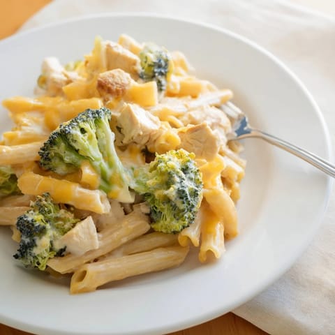 Steaming plate of Chicken Broccoli Cheddar Pasta, featuring golden penne noodles, sautéed chicken, and crisp broccoli, finished with a generous sprinkle of sharp cheddar.
