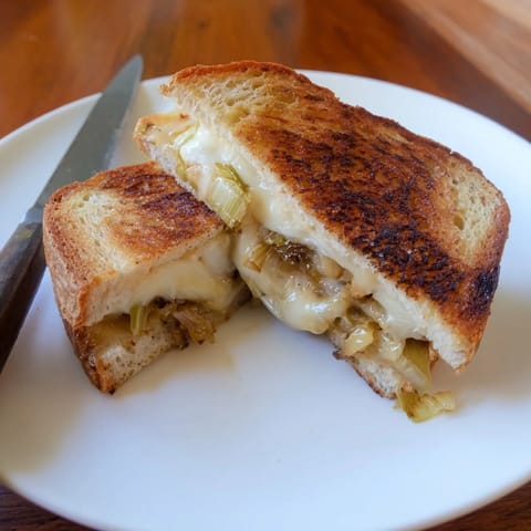 A close-up of the Havarti & Caramelized Leek Grilled Cheese reveals a gooey, cheesy pull between crispy bread.