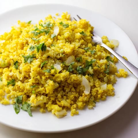 A bowl of fluffy, golden-yellow cauliflower rice seasoned with turmeric and cumin, topped with fresh parsley.  
