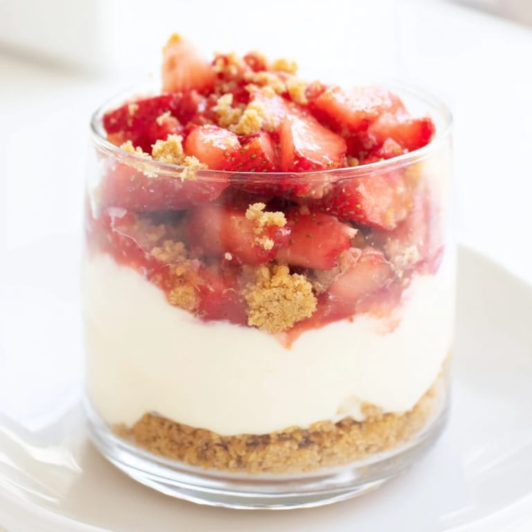 Elegant dessert: a layered strawberry cheesecake parfait with juicy strawberries and golden cookie crumbles.