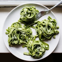 A vibrant green spinach pasta dough ball rests on a floured wooden countertop, ready for rolling.