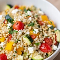Roasted Veggie Couscous Salad with colorful zucchini, bell peppers, and tomatoes on a white plate.