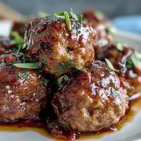 Slow Cooker Peach Glazed Meatballs simmer in a sweet and tangy sauce, garnished with fresh parsley for an easy party appetizer.