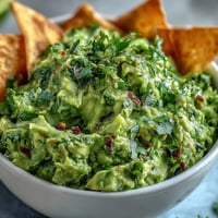 Vibrant edamame guacamole with creamy avocado, served alongside golden, crisp pita chips for a fresh, protein-packed snack.  