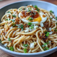 A steaming bowl of viral garlic butter ramen, glossy noodles coated in rich, savory sauce with a sprinkle of green onions and sesame seeds.